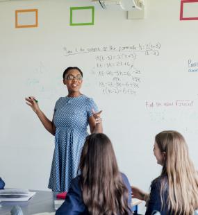 Women standing at a whiteboard educating a class of kids