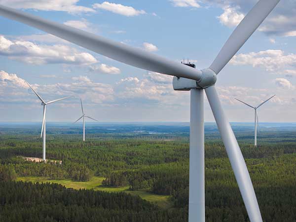 Close-up of a wind turbine with several others in the distance, all standing above a green forest landscape under a cloudy sky.