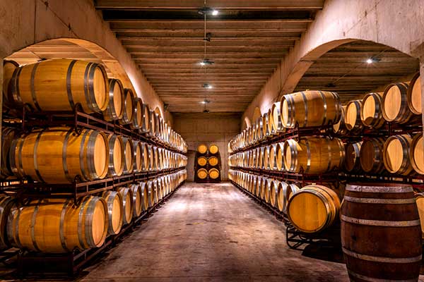 Rows of wooden whisky barrels stacked in a dimly lit cellar with arched ceilings and concrete floors.