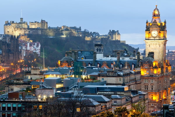 View of Edinburgh cityscape at dusk, featuring Edinburgh Castle on a hill and the Balmoral Hotel clock tower in the foreground.