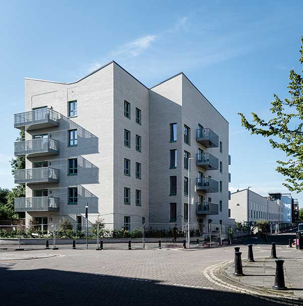 A modern white apartment building with balconies on a quiet street corner under a clear blue sky.