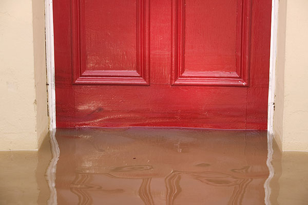 Brown floodwater pooled against a closed red door, partially submerging the bottom section of the door frame.