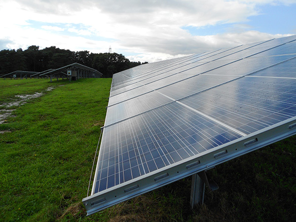 Rows of solar panels installed on a grassy field under a partly cloudy sky.