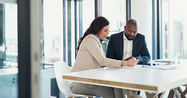 Two people sitting at a table in an office, reviewing documents together.