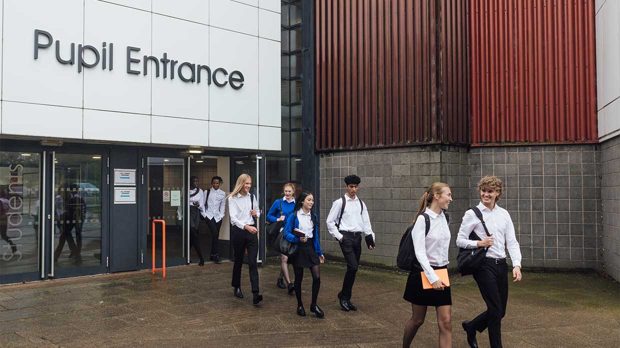 Students in uniform walking out of the school building through the "Pupil Entrance" doors.