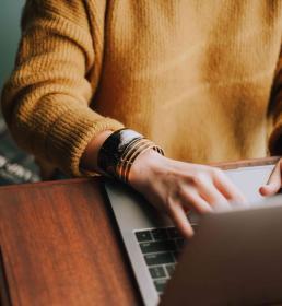 Person in a yellow jumper sat at a desk using a laptop
