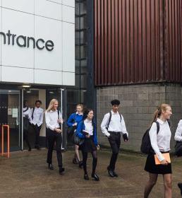 Students in uniform walking out of the school building through the "Pupil Entrance" doors.