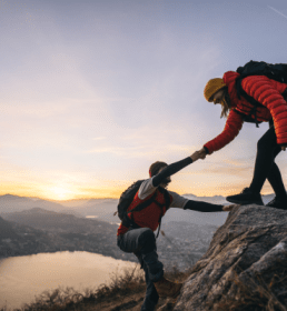 Two people supporting each other to climb a mountain