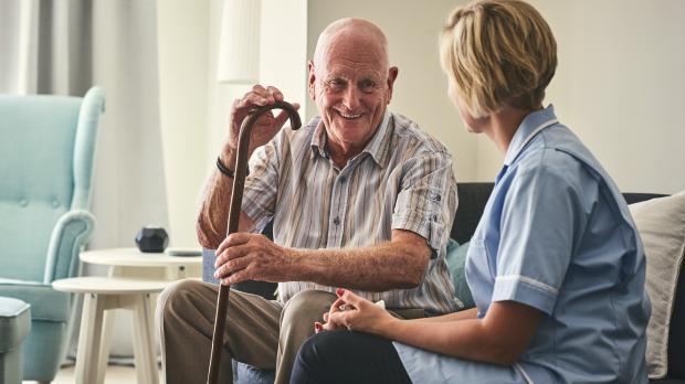 An older gentleman smiles as he sits with his carer