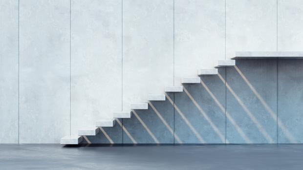 A modern flight of stairs with no riser or banister runs up the side of a building to a platform and casts shadows on the wall below
