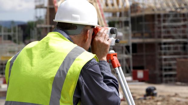 A surveyor looks through a theodolite on a house building site