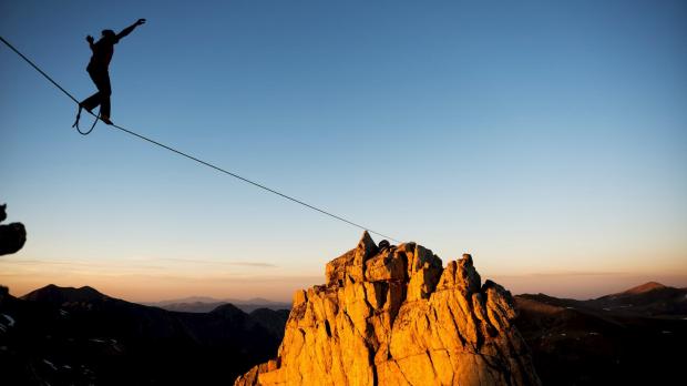 Tightrope walker walking across mountains at dusk