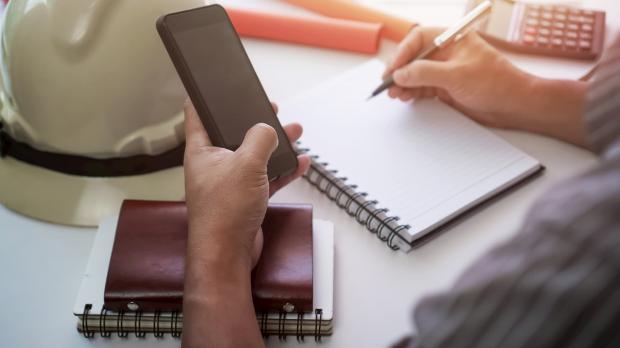 Man writing on notepad with phone in hand.