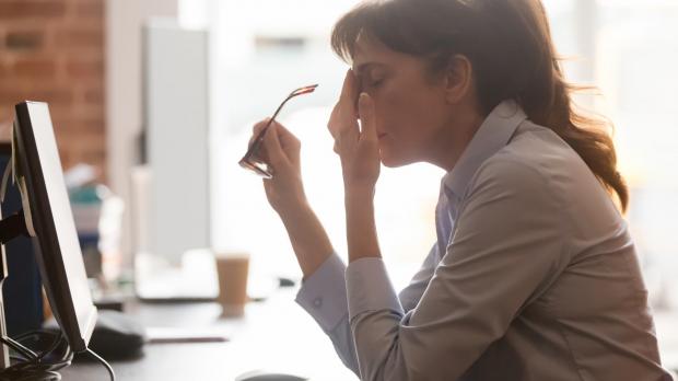 Woman sat at her desk rubbing her forehead.