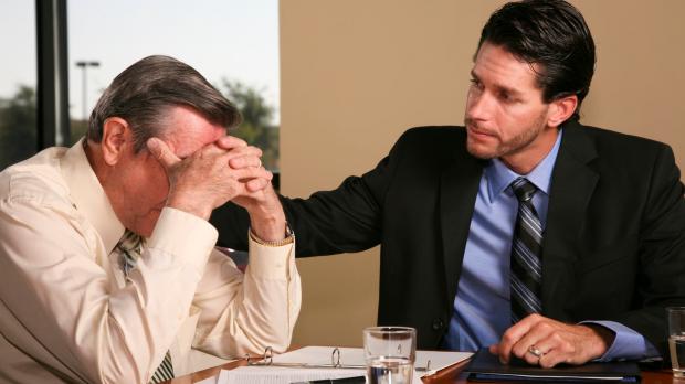 Older man with head in hands being comforted by younger male work colleague