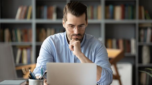Man in a blue shirt studying his work laptop