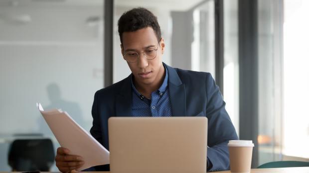 Male in suit sitting at desk with laptop and papers