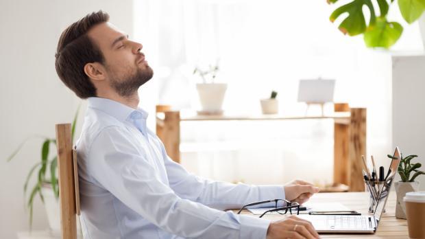 Man at laptop leaning back with eyes closed