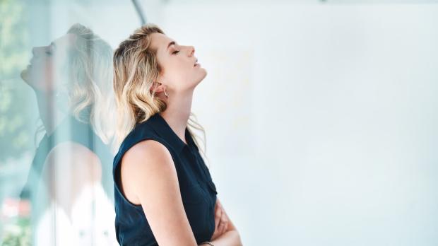 Woman leaning back against a window, eyes shut, arms folded