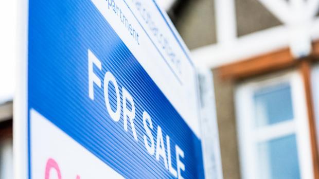 For sale sign with house in the background