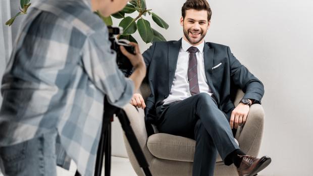 Businessman in chair with woman capturing him on video