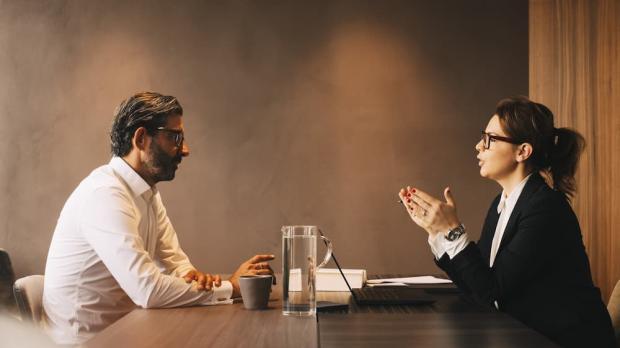 Two people sitting across from each other at a table with laptops in front of them.