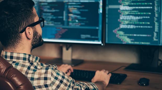 A seated man looking at two computer screens