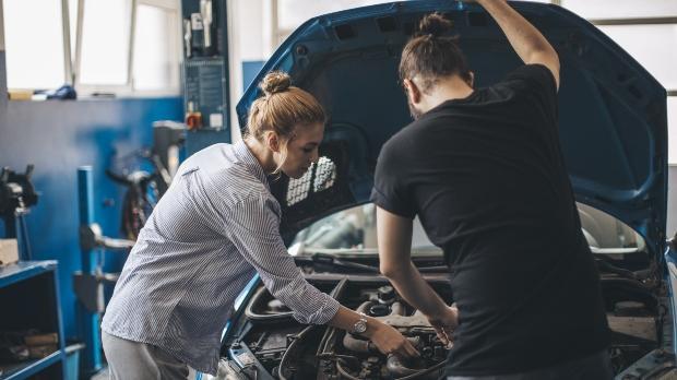 mechanic and customer looking under car hood in workshop