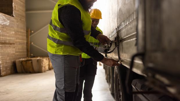 Two young warehouse workers tying down a truck trailer with ratchet straps