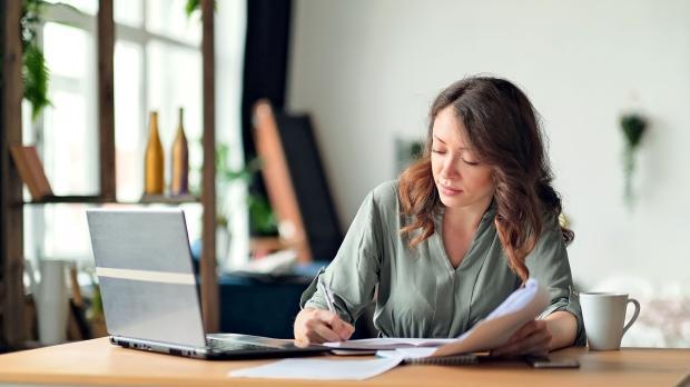 Woman writing at desk in front of laptop
