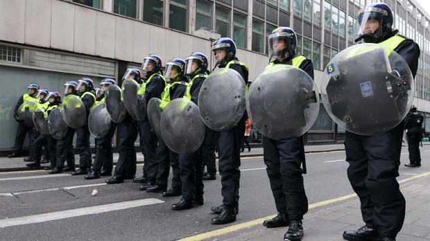 UK riot police with shields wearing helmets lined up ready