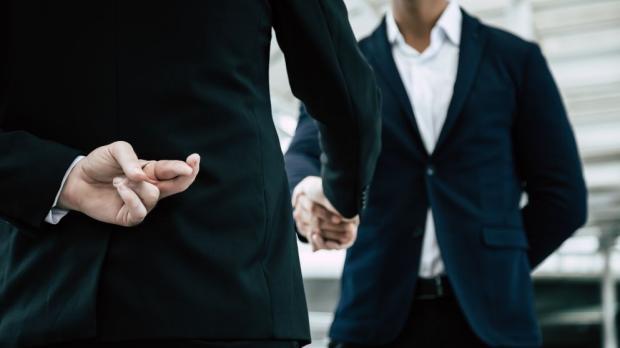 two businessmen shaking hands, one with fingers crossed behind their back