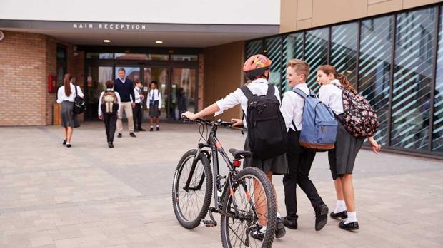 Three school age children, one with a bike, walking into school