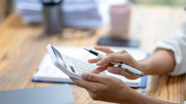 A woman is using a calculator and pen on a desk. She is focused on her work