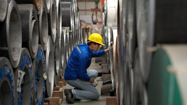 Industrial worker inspecting inside a large metal tube in a factory wearing safety helmet and gloves