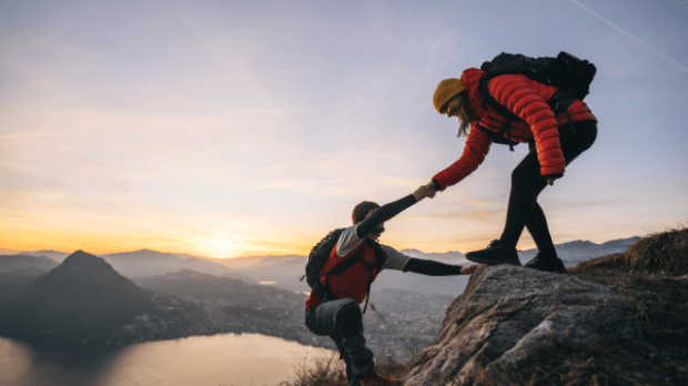 Two people supporting each other to climb a mountain