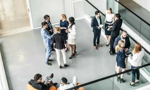 Young professionals stand talking in small groups in the foyer of an office building