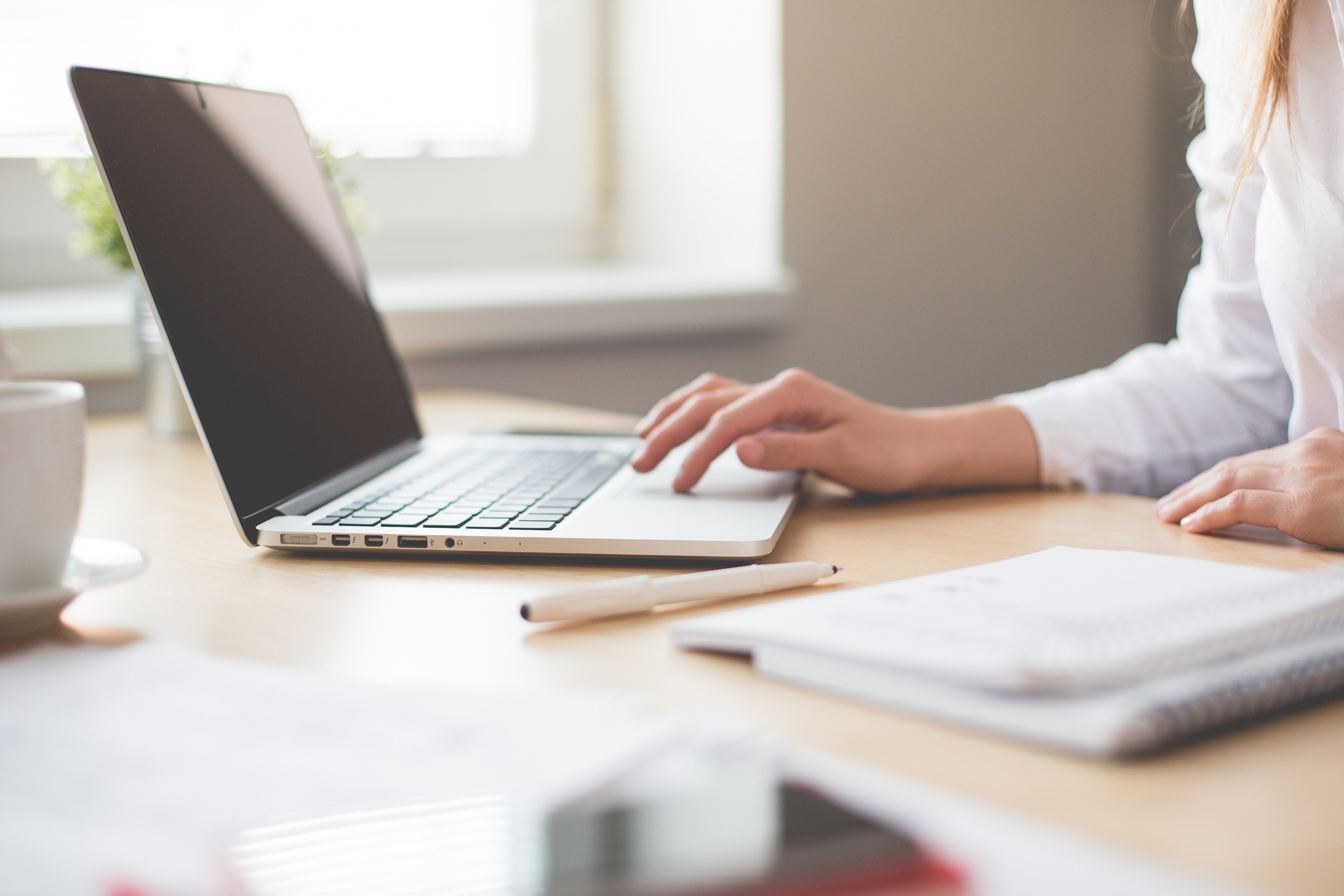 A businesswoman in a white shirt sits at a desk using a laptop