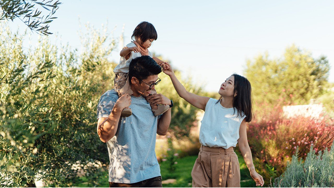 A man outside with child on his shoulders and a woman next to them holding hands with the child