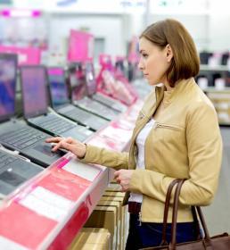 A lady in a tan leather jacket tries out a new laptop in a technology store