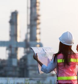 A female engineer holds up blueprints as she surveys a power station from a distance