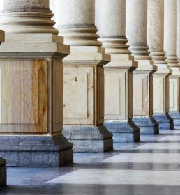 A row of marble columns with the sunlight shining through, casting shadows on the floor