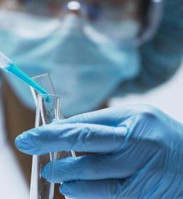 A lab technician wearing blue gloves pipettes blue liquid into a test tube