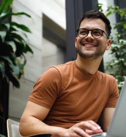 young man sitting in the armchair in the modern green building lobby and working on his laptop.
