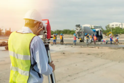 A surveyor on a building site looks through a theodolite
