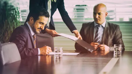 Merger being signed by two guys at a boardroom table