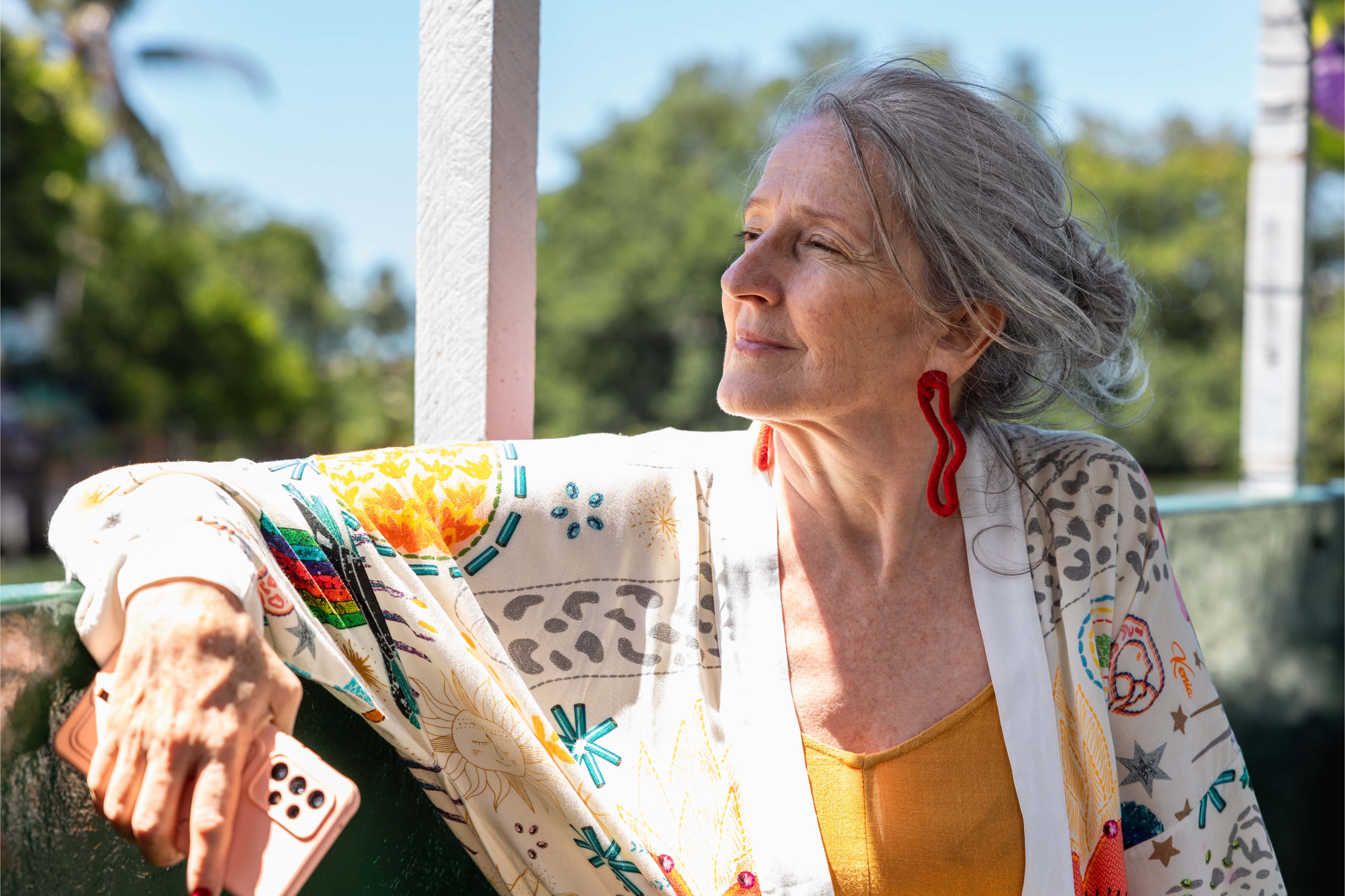 Smiling older woman in colourful clothing relaxing outdoors with sunlight on her face