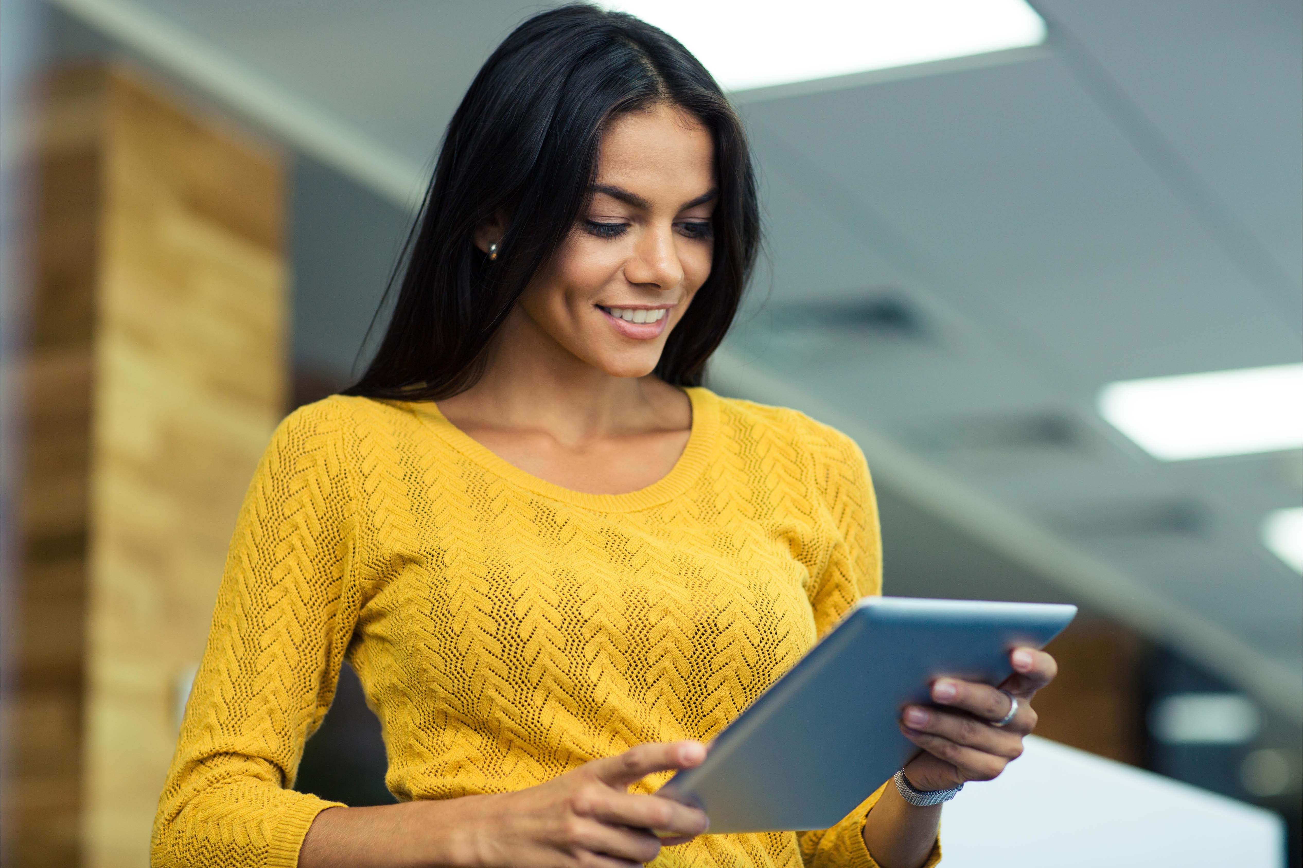 Smiling woman in a yellow top working on a tablet in a contemporary office space