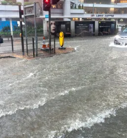 A woman tries to cross a heavily flooded high street as a car drives past in deep water