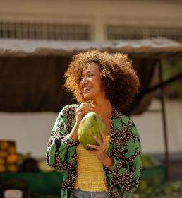 Happy woman holding a coconut with a straw while standing at an outdoor fruit market